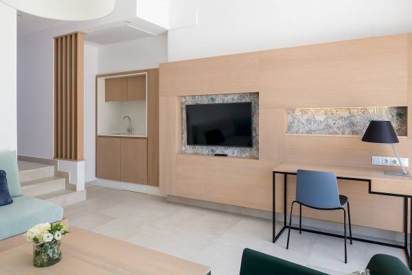 Wohnbereich des Plus Fariones Suite Hotels mit Couch, Tisch, Fernseher und Schreibtisch.