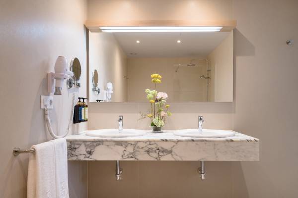 Badezimmer im Plus Fariones Suite Hotel mit Marmorwaschbecken und Spiegeln.