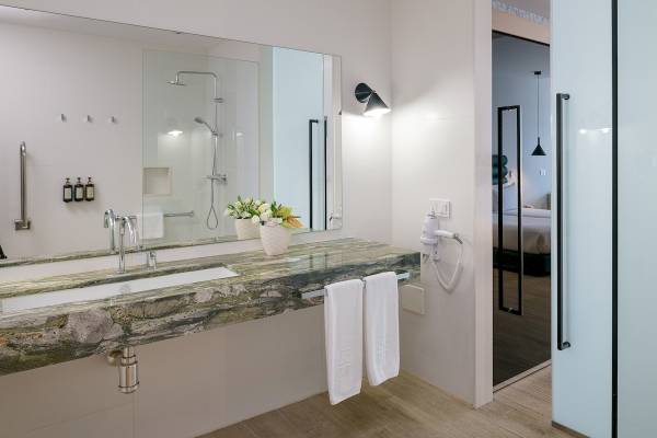 Badezimmer im Plus Fariones Suite Hotel mit Marmorwaschtisch, Spiegel und Dusche.
