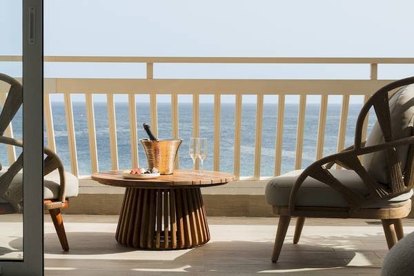 Terrasse des Plus Fariones Suite Hotel mit Blick auf das Meer und zwei Stühlen, einem Tisch mit Flasche und Gläsern.