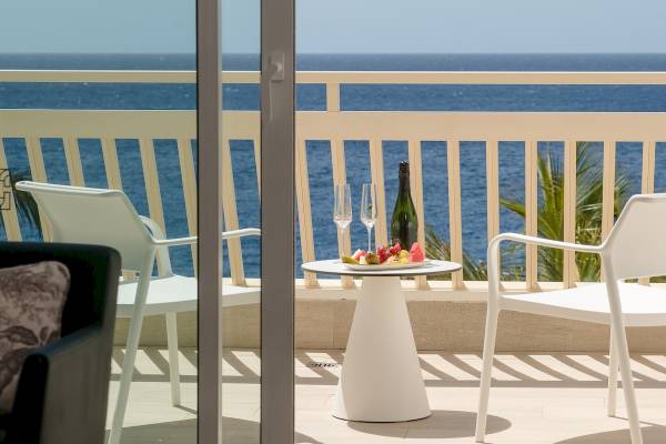 Terrasse mit Meerblick im Plus Fariones Suite Hotel mit Obstteller, Weinflasche und Gläsern.