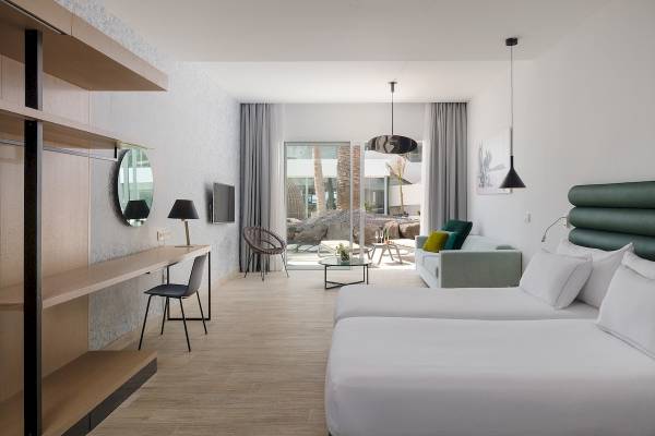 Innenraum des Plus Fariones Suite Hotel mit zwei Betten, Wohnzimmerbereich und Blick durch Glastüren.