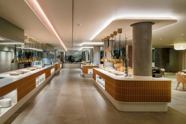 Innenansicht des Restaurants im Plus Fariones Suite Hotel mit Buffettischen und hängenden Lampen.