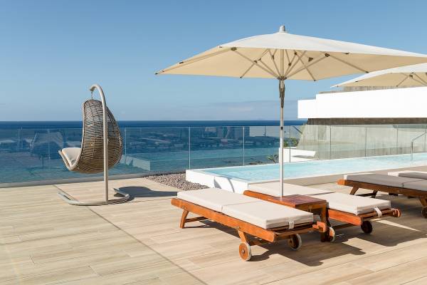 Terrasse des Plus Fariones Suite Hotels mit Liegen und Sonnenschirmen und Meerblick.
