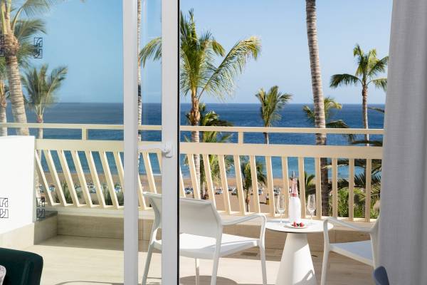 Terrasse mit Meerblick im Plus Fariones Suite Hotel mit weißen Möbeln und Palmen