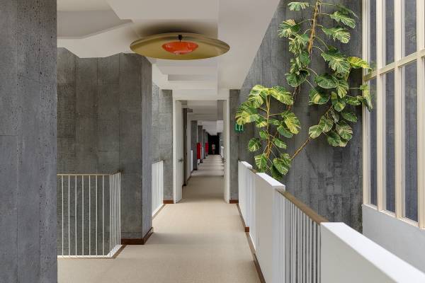 Innenansicht des Flurs im Plus Fariones Suite Hotel mit grauen Wänden, beigem Teppich und einer großen orangefarbenen Lampe.
