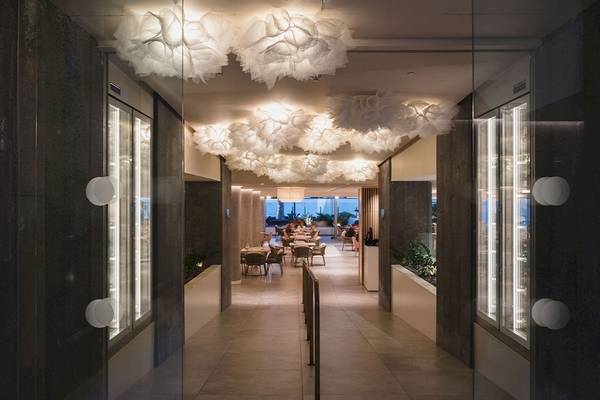 Innenbereich des Plus Fariones Suite Hotels mit geometrischen Deckenleuchten und Tischen im Freien.