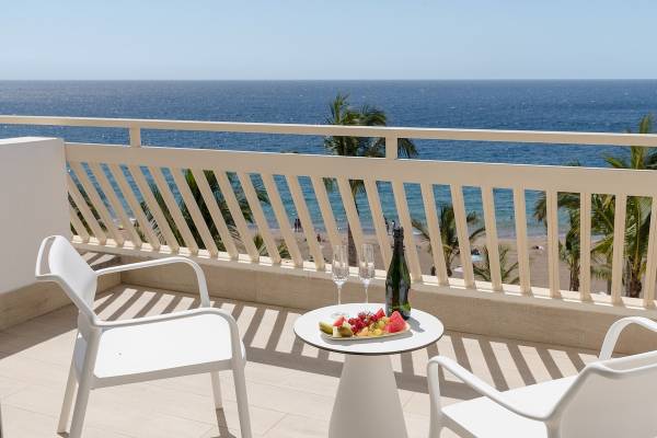 Balkon im Plus Fariones Suite Hotel mit Blick auf den Ozean und Früchten auf dem Tisch.