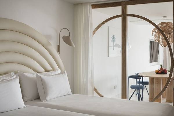 Schlafzimmer im Plus Fariones Suite Hotel mit zwei Betten, weißen Kissen, einem Lampenschirm und einem Ausblick auf einen Esstisch mit Früchten.