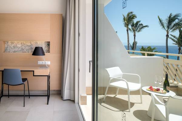 Innenansicht des Plus Fariones Suite Hotels mit Schreibtisch und Blick auf den Balkon.