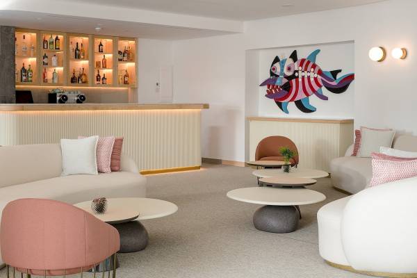 Loungebereich des Plus Fariones Suite Hotels mit Couch, Tischen und einer bunten Wandmalerei.