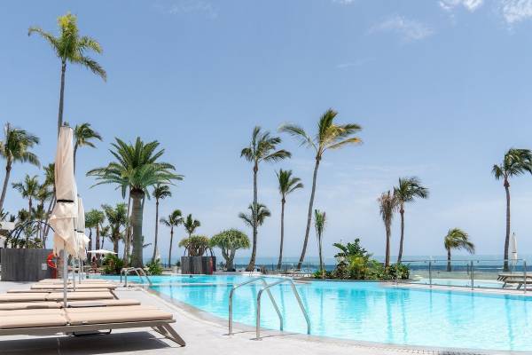 Ein Swimmingpool mit Liegestühlen und Palmen am Strand