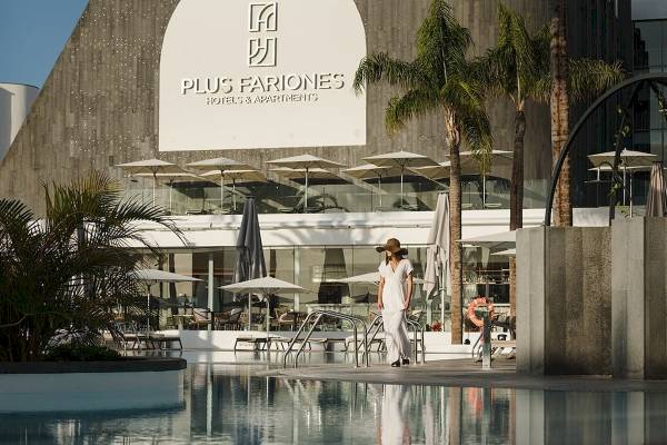 Eine Frau in einem weißen Kleid und Hut geht vor dem Plus Fariones Suite Hotel am Pool entlang.