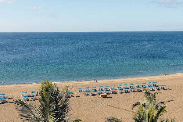 Aussicht auf den Strand des Plus Fariones Suite Hotel mit blauen Sonnenschirmen und Palmen