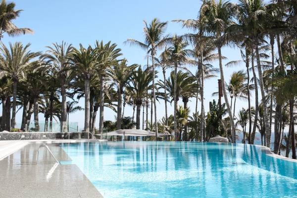 Pool des Fariones Hotels mit Palmen und Meer im Hintergrund