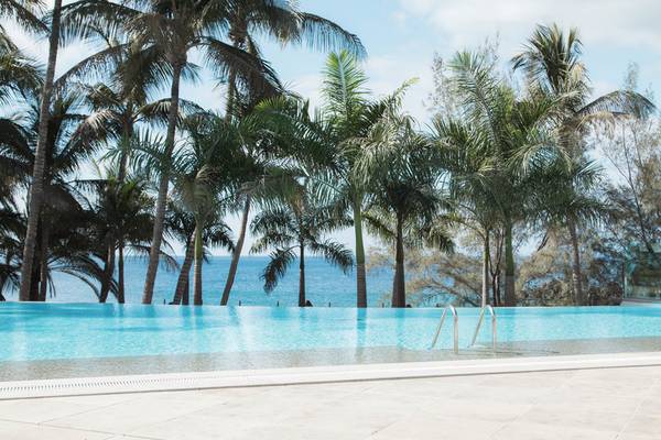 Ein Swimmingpool des Fariones Hotel mit Blick auf das Meer und Palmen im Hintergrund.