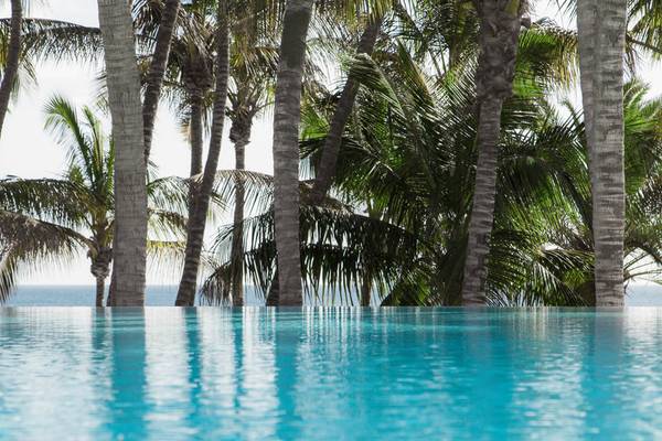 Ein kristallklarer Pool im Fariones Hotel mit Palmen im Hintergrund, die zur Küste führen.