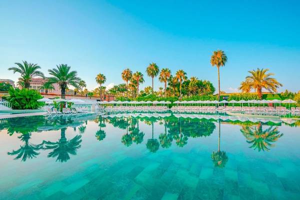 Außenpool des Kirman Leodikya Resorts mit weißen Sonnenliegen und Palmen im Hintergrund