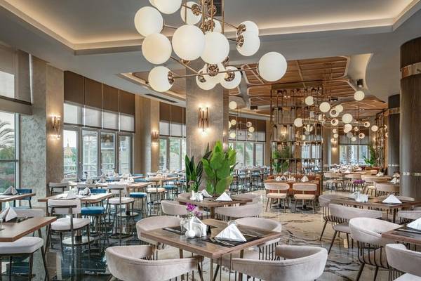 Innenbereich des Restaurants im Kirman Leodikya Resort mit modernen Möbeln, hängenden Kronleuchtern und großen Fenstern.