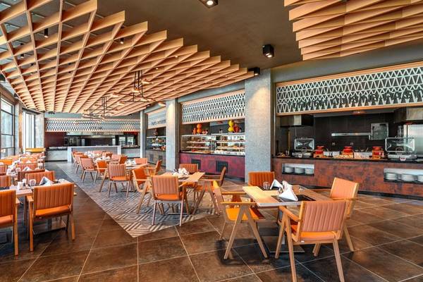 Innenbereich des Restaurants im Kirman Leodikya Resort mit modernen Holzmöbeln und einer offenen Küche.