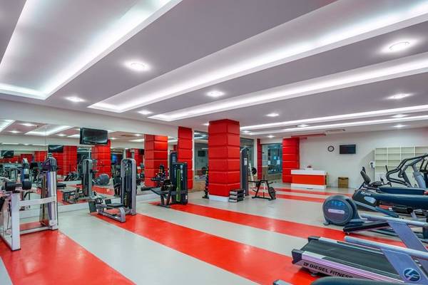 Fitnesscenter im Kirman Leodikya Resort mit roten und weißen Bodenstreifen und verschiedenen Fitnessgeräten.