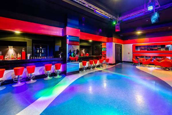 Innenbereich einer Hotelbar mit roten Stühlen, einer Theke und bunten Lichtern