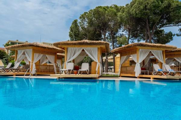 Drei strohgedeckte Loungehütten am Pool des Ducale Lara Hotels mit weißen Vorhängen und Sonnenliegen.
