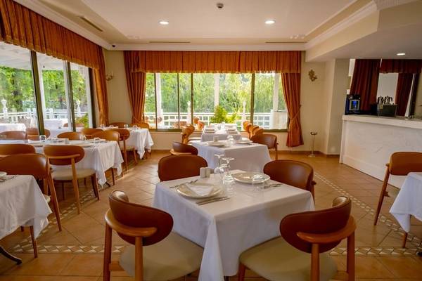 Innenansicht des Restaurants im Ducale Lara Hotel mit gedeckten Tischen und Fenstern, die auf einen Garten blicken.