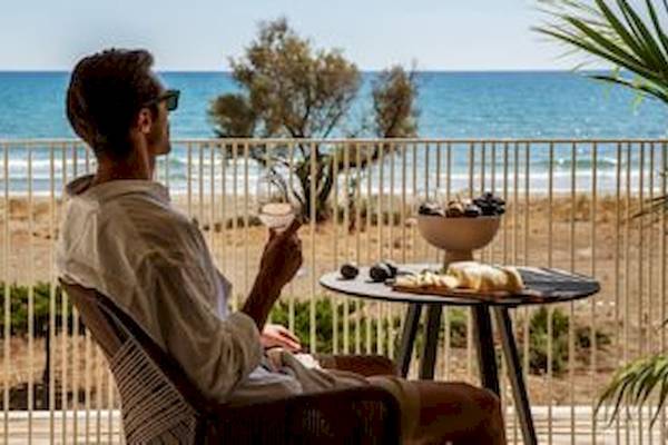 Ein Mann sitzt auf einem Balkon mit Blick auf das Meer und hält ein Glas Wein.