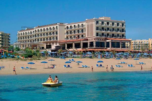 Constantinos the Great Beach Hotel am Strand mit vielen Liegen und Sonnenschirmen.