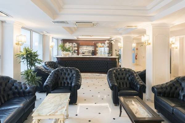 Lobby des Baia Imperiale Hotels mit schwarzen Ledersofas, weißen Fliesen und einer Bar.