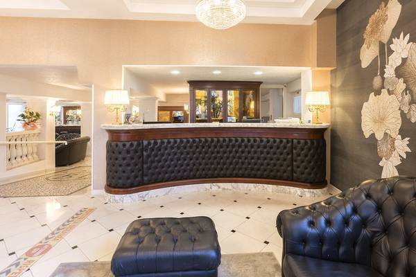 Empfangsbereich des Baia Imperiale Hotels mit Ledersofas, Empfangstresen und Kronleuchter.