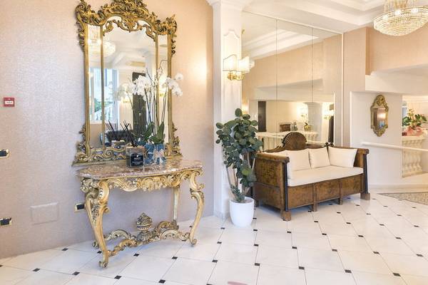 Ein eleganter Eingangsbereich des Baia Imperiale Hotels mit einem goldenen Spiegel, einem Marmortisch, einer Pflanze und einem Sofa.