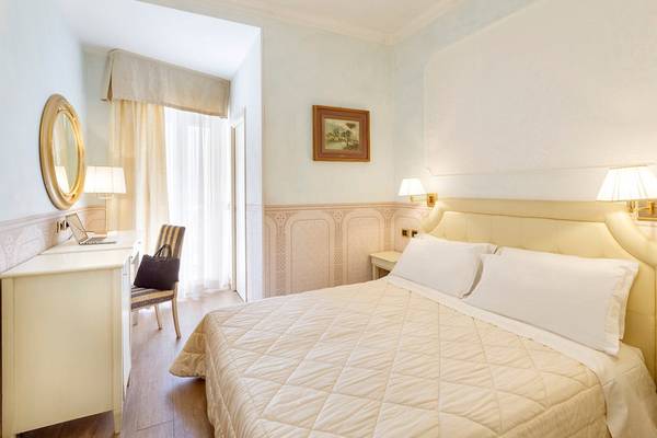 Innenansicht eines Zimmers im Baia Imperiale Hotel mit einem Bett, Schreibtisch und Lampe.