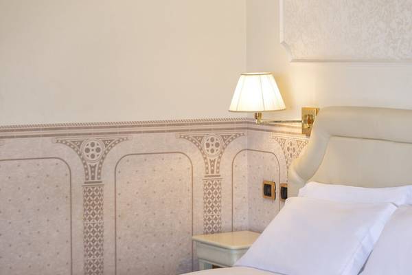 Schlafzimmer im Baia Imperiale Hotel mit Bett, weißen Kissen und Wandbeleuchtung.