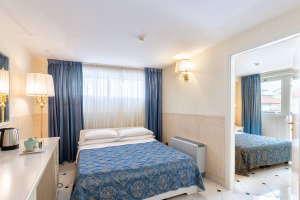 Ein elegantes Hotelzimmer im Baia Imperiale Hotel mit zwei Betten, blauen Vorhängen und einem Schreibtisch.