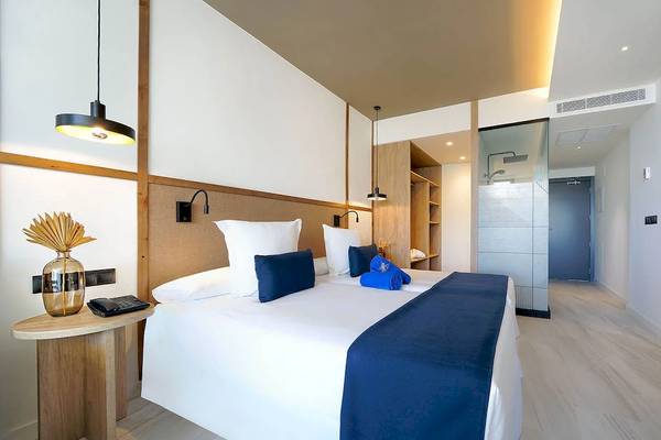 Innenansicht eines Hotelzimmers im H10 Costa Mogan mit einem Doppelbett, Holzmöbeln und modernen Beleuchtungskörpern.