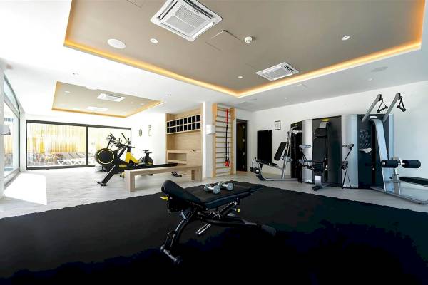 Fitnessbereich im H10 Costa Mogan Hotel mit verschiedenen Trainingsgeräten und einer Glaswand.