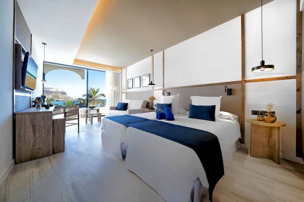 Innenansicht des H10 Costa Mogan Hotelzimmers mit zwei Betten, Meerblick und moderner Einrichtung.