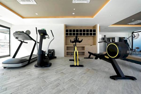 Fitnessbereich im H10 Costa Mogan Hotel mit mehreren Trainingsgeräten und einem Holzschrank.