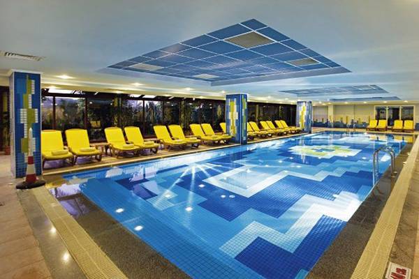 Innenpool des Belek Beach Resort Hotel mit gelben Liegestühlen und blau-weißen Bodenfliesen.