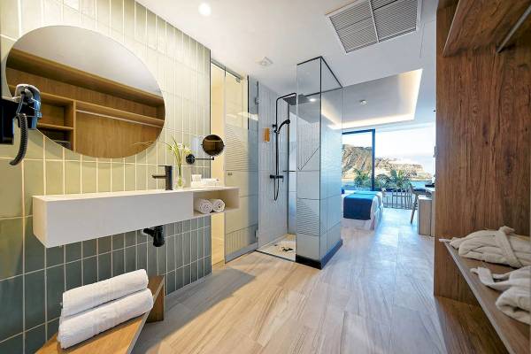 Badezimmer im H10 Costa Mogan Hotel mit grünen Kacheln, weißem Waschbecken, Regendusche und Ausblick auf das Meer.