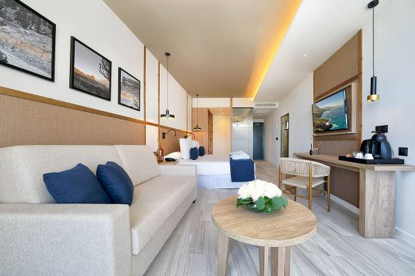 H10 Costa Mogan Hotel Zimmer mit Bett, Sofa, Tisch und Fernseher.