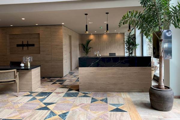 Empfangsbereich des H10 Costa Mogan Hotels mit Marmorboden, Holzmöbeln und Pflanzen.