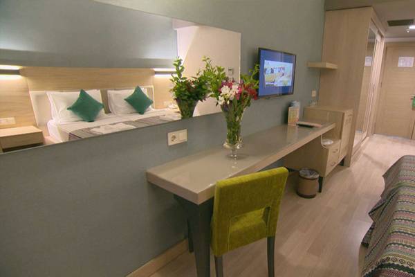 Innenansicht eines Zimmers im Belek Beach Resort Hotel mit Schreibtisch, grünem Stuhl und Fernseher.