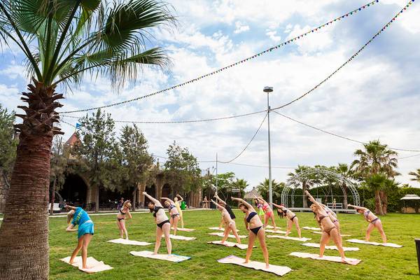Yoga Kurs im Freien am Belek Beach Resort Hotel mit vielen Frauen in Bikinis auf Yogamatten.