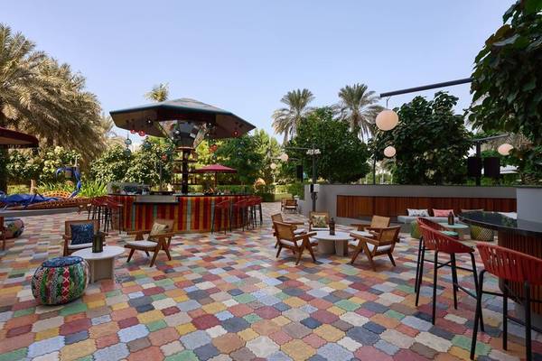 Außenbereich des W Dubai - Mina Seyahi Hotels mit buntem Boden, Tischen, Stühlen und einer Bar.