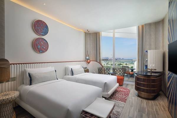 Innenansicht eines Zimmers im W Dubai - Mina Seyahi Hotel mit zwei Betten, Ausblick auf die Stadt und modernem Interieur.