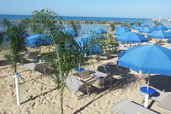 Strand des Acacia Marina Hotels mit vielen blauen Sonnenschirmen und Liegen