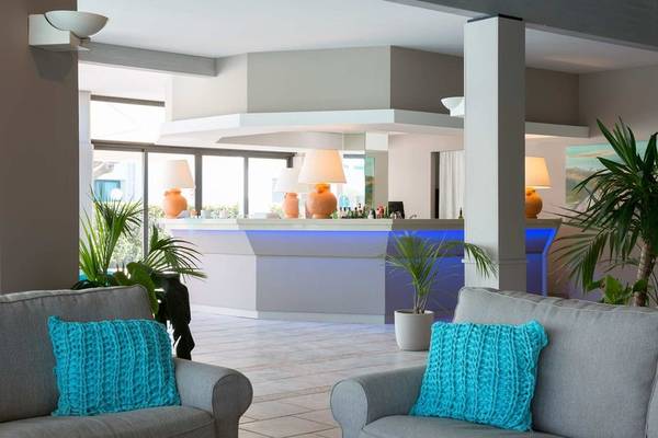 Empfangsbereich des Acacia Marina Hotels mit modernen Möbeln, orangefarbenen Lampen und Pflanzen.